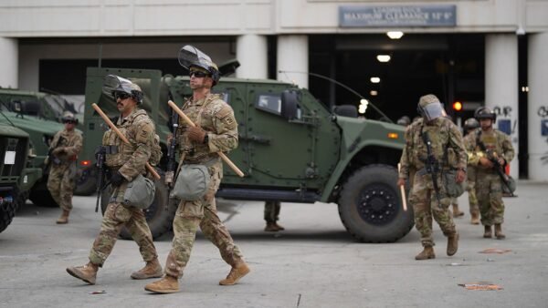 "U.S. Marines Make History by Detaining First Civilian Protester Amid Nationwide Demonstrations in LA" 5 U.S. National Guard troops walking by vehicle